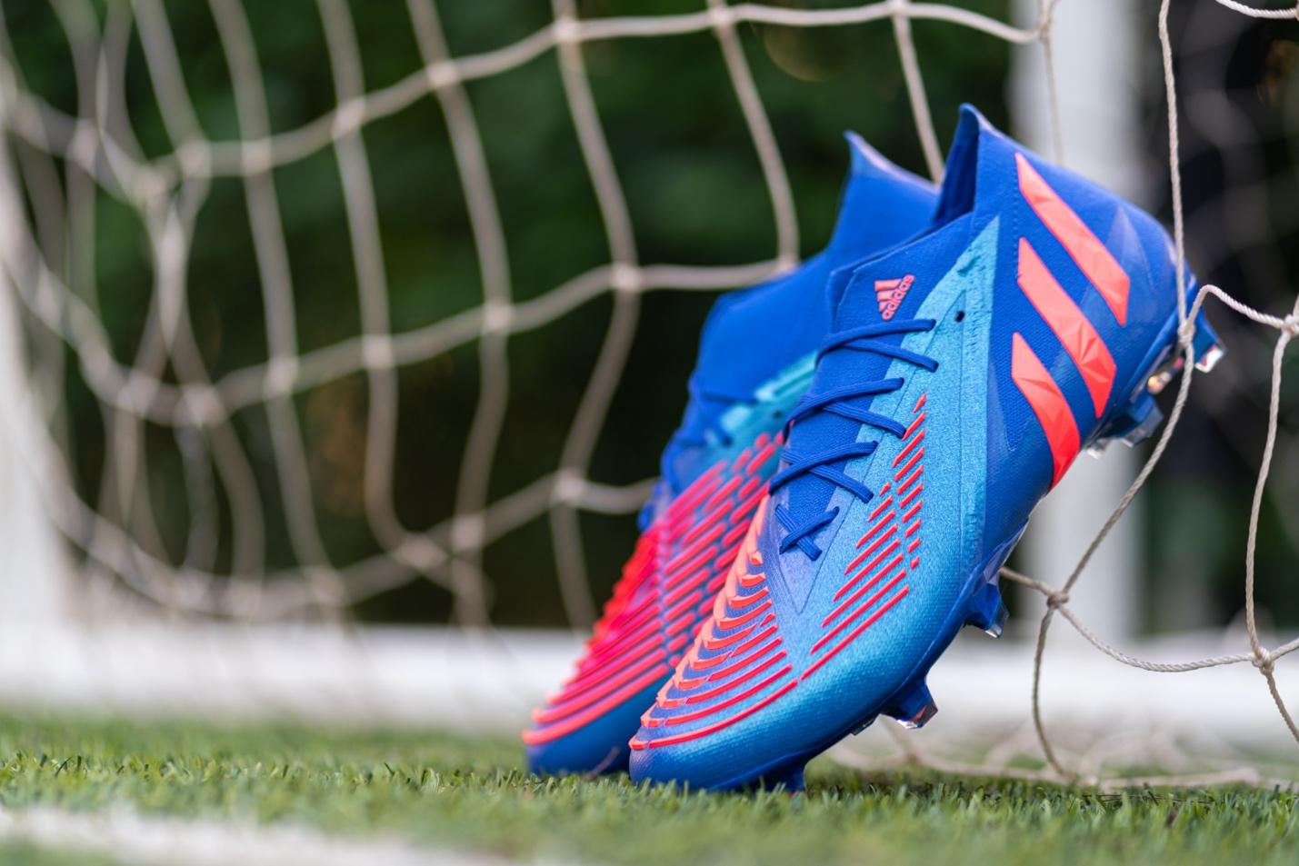 A pair of soccer shoes on the ground near a net.